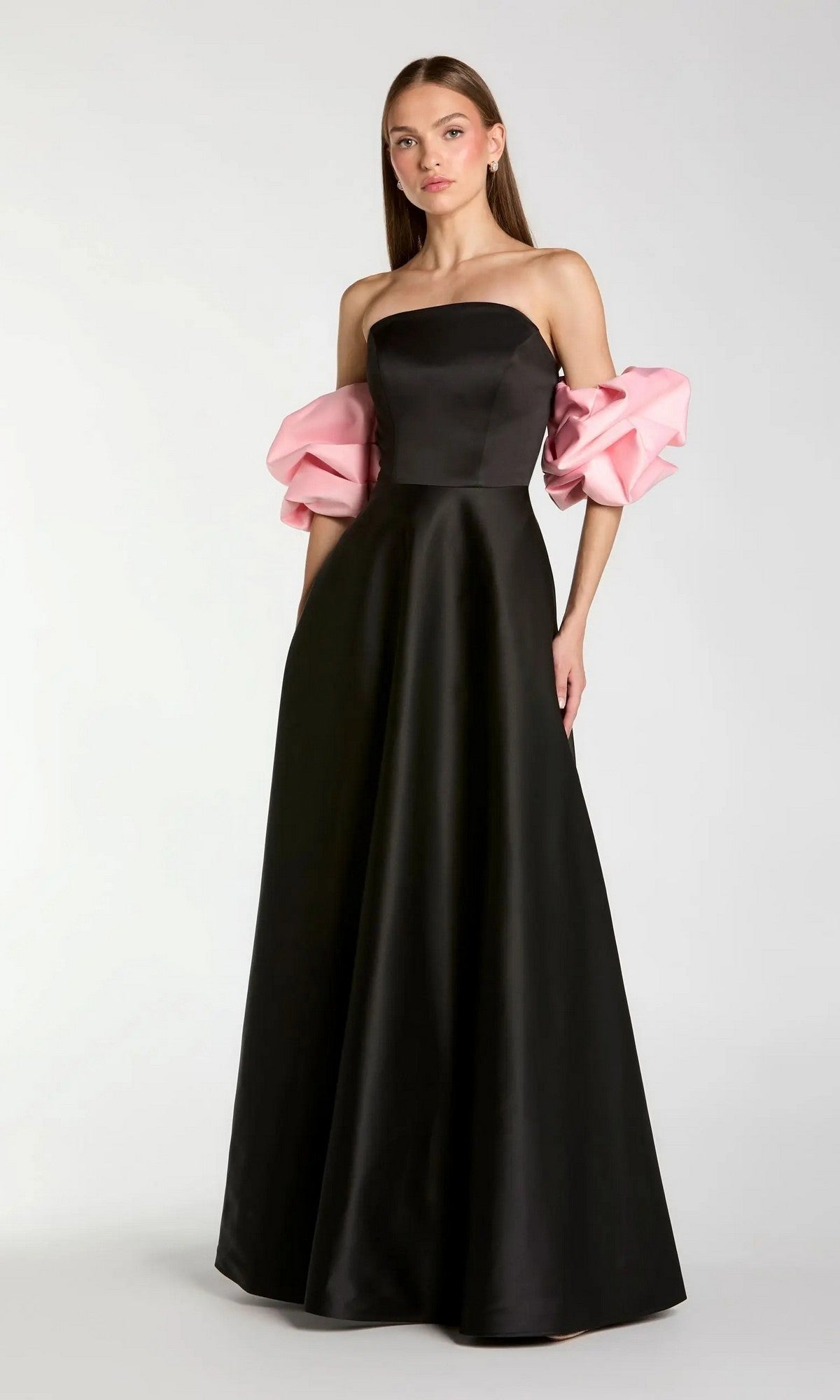 A woman wearing the Long Formal Dress: Mac Duggal 21241 in Black Pink, featuring a strapless satin gown with voluminous pink puff sleeves, stands against a plain light background.